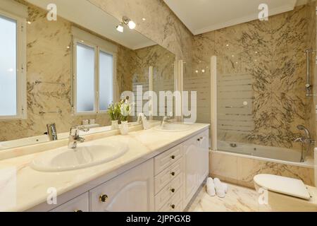 Badezimmer mit langer Marmorplatte mit zwei Waschbecken, großem rahmenlosen Spiegel an der Wand und Marmorfliesen an Wänden und Böden Stockfoto