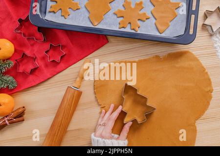 Frauenhände schneiden Baumform aus dem Lebkuchenteig, Draufsicht. Weihnachtsbacken. Stockfoto