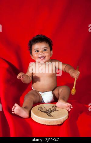 Happy Native American Baby spielt eine traditionelle Handtrommel, die an Festtagen verwendet wird und tanzt Stockfoto