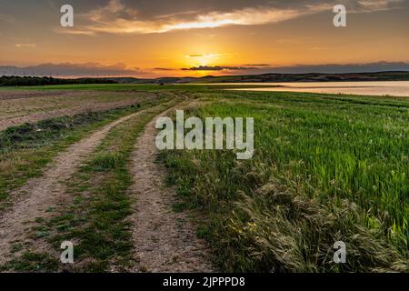 Sonnenuntergang auf dem Land, mit Windmühlen im Hintergrund, einem Stausee und einer Straße im Vordergrund Stockfoto