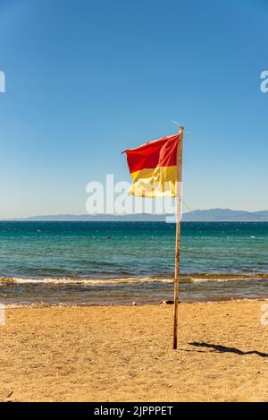 Rettungsschwimmer-Symbol am Strand, Rettungsschwimmer-Flagge winkt im Wind, um die Menschen zu informieren, gelbe rote Flagge und das Meer im Hintergrund Stockfoto