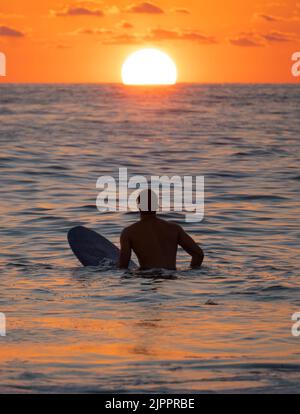 Silhouette des Surfers, der auf der Schlange auf eine Welle bei Sonnenaufgang oder Sonnenuntergang wartet Stockfoto