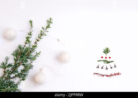 Weihnachtsbaum und grüner Zweig mit Girlande-Kugeln auf weißem Hintergrund als Symbol des neuen Jahres. Der Baum besteht aus Zweigen aus Thuja, Baumwolle, rotem Herz Stockfoto