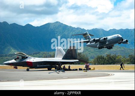 Eine US Air Force C-17 Globemaster III hebt am 12. August 2022 als Wartungspersonal einen F-22 Raptor während der Kaneohe Bay Air Show auf der Marine Corps Base Hawaii ab. Beide Flugzeuge sind der Joint Base Pearl Harbor-Hickam zugeordnet und werden von Mitgliedern der Hawaii Air National Guard betrieben. Die Veranstaltung wurde abgehalten, um die langjährigen Beziehungen des Militärs zur lokalen Gemeinschaft zu feiern und der Öffentlichkeit die Gelegenheit zu geben, die Fähigkeiten der gemeinsamen Truppe zu erleben. (USA Foto der Air National Guard von Staff Sgt. John Linzmeier) Stockfoto