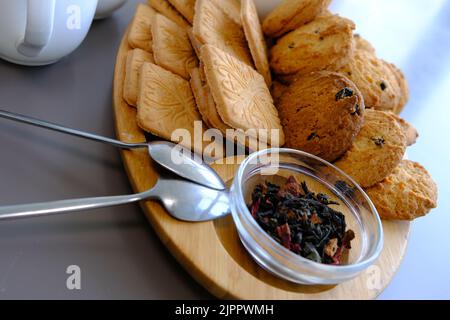 Ein leckerer Snack zwei Tassen schwarzen Tee und eine Platte mit Haferflocken Cookies ein Holzbrett auf dem grauen Hintergrund, Blatt Tee Stockfoto