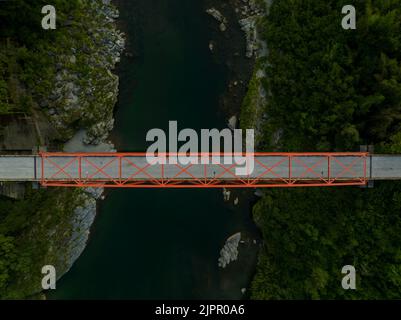 Luftaufnahme der leeren roten Brücke über den kleinen Fluss und die felsige Landschaft in der Abenddämmerung Stockfoto
