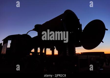 Die Silhouette einer alten Lokomotive in der Dämmerung auf dem Eisenbahnfriedhof von Uyuni, Potosi, Bolivien. Stockfoto