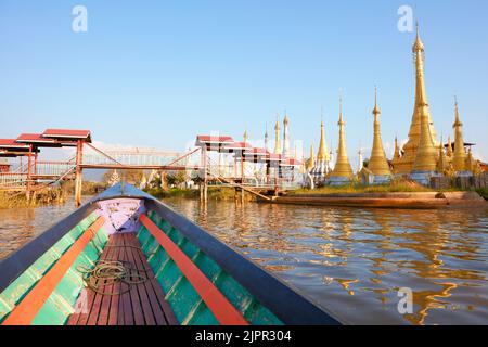 Ein Holzboot fährt auf Inle Lak mit goldenen buddhistischen Pagoden im Hintergrund, Myanmar. Stockfoto