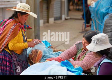 Eine bolivianische Chola-Frau kauft Brot an einem Stand auf dem Straßenmarkt an der Copaana, dem Titicacasee, Provinz La Paz, Bolivien. Stockfoto