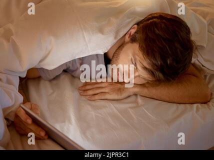 Mann, der sich auf einem digitalen Tablet im Bett entspannt und in sozialen Netzwerken oder im Internet surft. Männer sind süchtig nach Technologie-Scrollen auf dem Handy bei Stockfoto