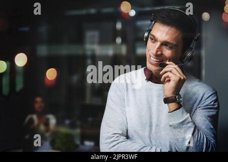 Also... wie kann ich Ihnen helfen. Ein hübscher junger Geschäftsmann, der nachdenklich aussieht und spät in einem Callcenter arbeitet. Stockfoto