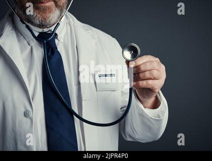 Das Herz spricht für sich selbst. Studioaufnahme eines nicht erkennbaren männlichen Arztes, der ein Stethoskop vor einem dunklen Hintergrund hält. Stockfoto