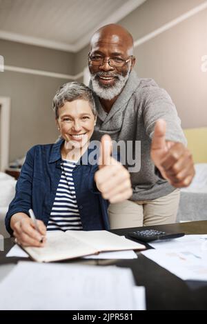 Unsere Einsparungen sind sortiert. Porträt eines älteren Ehepaars, das Ihnen die Daumen nach oben gibt, während Sie zu Hause an ihren Finanzen arbeiten. Stockfoto
