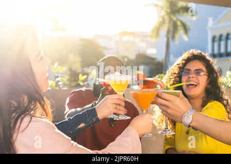 Fröhliche junge Freunde, die draußen Spaß haben und zusammen mit Cocktails toasten. Konzentrieren Sie sich auf die Brille - Freundschaftskonzept. Stockfoto