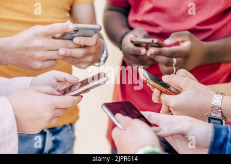 Gruppe junger Menschen, die ihre Telefone im Freien benutzen. Bildung, Technologie und Glückskonzept Stockfoto