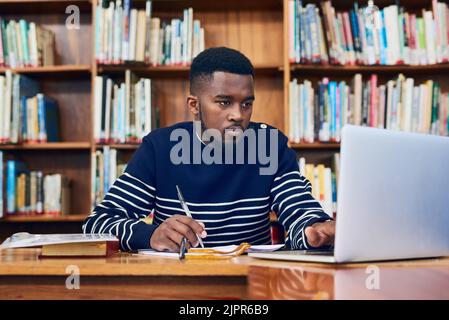 Er recherchiert, um Bestnoten zu erhalten. Ein Student der Universität forscht auf einem Laptop. Stockfoto