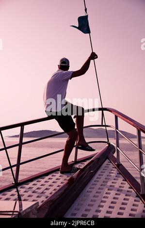 Mann, der auf einem Zaun eines traditionellen hölzernen Segelbootes sitzt Stockfoto
