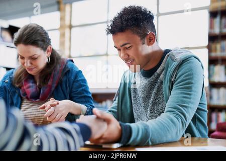 Studenten, die beten, werden nie scheitern. Eine Gruppe von Studenten beten zusammen, während sie in einer Bibliothek sitzen. Stockfoto