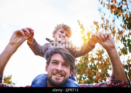 Hoch auf den Schultern des Daddys. Aufnahme eines hübschen jungen Mannes, der im Herbst seinen Sohn im Freien huckepack. Stockfoto