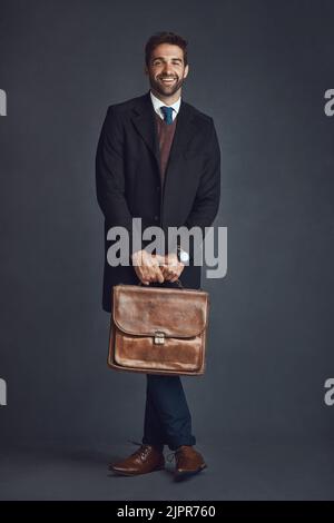 Mit diesem Style sind Sie auf alles vorbereitet. Studioporträt eines stilvoll gekleideten jungen Mannes, der eine Tasche vor grauem Hintergrund trägt. Stockfoto