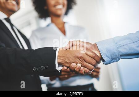 Mit einem weiteren Partner an Bord. Zwei unkenntliche Geschäftsleute, die sich in einem Büro die Hände schütteln. Stockfoto