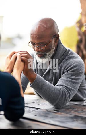 Verbringen Sie ein wenig Zeit im Gebet. Ein älteres Paar hält die Hände im Gebet, während es draußen sitzt. Stockfoto