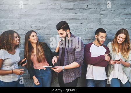 Bleiben Sie mit den Menschen in Verbindung, die am wichtigsten sind. Eine Gruppe junger Freunde, die ihre drahtlosen Geräte gemeinsam im Freien nutzen. Stockfoto