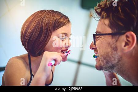 Ein Vater und seine kleine Tochter putzen sich zu Hause die Zähne zusammen. Stockfoto