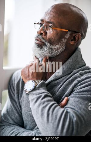 Er verbringt viel Zeit tief in Gedanken. Ein gutaussehender älterer Mann, der nachdenklich aussieht, während er in seinem Haus sitzt. Stockfoto