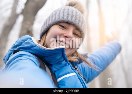 Junge Wanderer Mädchen in blauem Mantel und Winterhaube nimmt ein Selfie im Wald - Abenteuer-Konzept Stockfoto