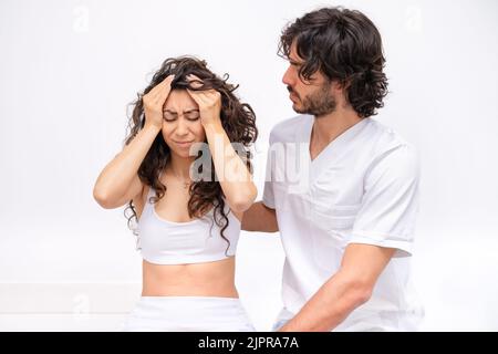 Frau in der Klinik in Absprache mit einem jungen Physiotherapeuten Arzt und Beschwerden über Kopfschmerzen - Gesundheitskonzept Stockfoto