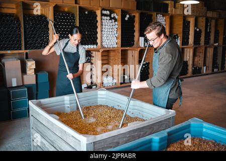 Trauben für die Weinherstellung in Keller, Weingut und Destillerie zerkleinern. Industriemitarbeiter, Winzer und Arbeiter mit Presswerkzeug in einem Tank zu mischen Stockfoto