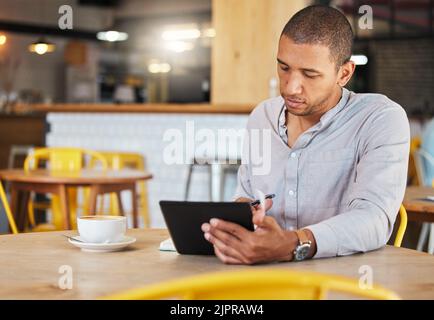 Seriöser freiberuflicher Geschäftsmann, der in einem Café arbeitet und für sein Startup Remote-Unternehmen arbeitet. Junger männlicher Unternehmer mit einer Tablette, die Wachstum plant Stockfoto