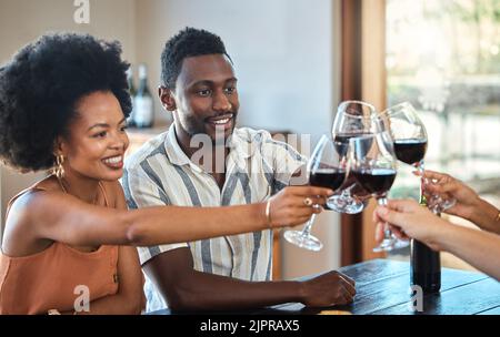 Das schwarze Paar feiert seinen Jahrestag mit Freunden, toast und trinkt Rotwein. Glückliche Freundin und Freund beim Familientreffen Stockfoto