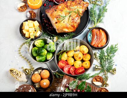 Köstlicher weihnachtlicher Esstisch mit gebratenem Fleisch, Kartoffeln, Vorspeisen und Desserts. Urlaubskonzept. Draufsicht auf grauem Hintergrund. Urlaub CO Stockfoto