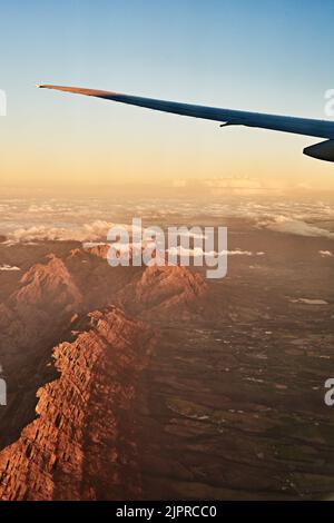 Hoch über den Bergen. Aus einem Flugzeugfenster eine Aufnahme aus dem hohen Winkel der Aussicht. Stockfoto