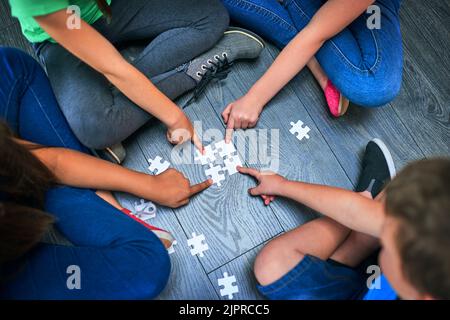 Das perfekte Spiel, um den Lernprozess zu unterstützen. Eine Gruppe von Kindern, die ein Spiel mit Puzzles auf dem Boden halten, in einem Hochwinkel. Stockfoto