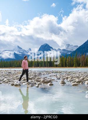 Icefields Parkway mit Herbstbäumen und schneebedeckten, nebligen Bergen in Jasper Canada, Alberta. Junge Männer wandern am Icefield Parkway in Kanada an einem Fluss entlang Stockfoto