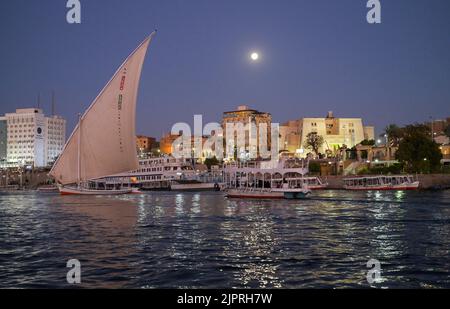 Vollmond, Segelschiff und Ausflugsboote auf dem abendlichen Nil in der Nähe von Assuan, Ägypten Stockfoto