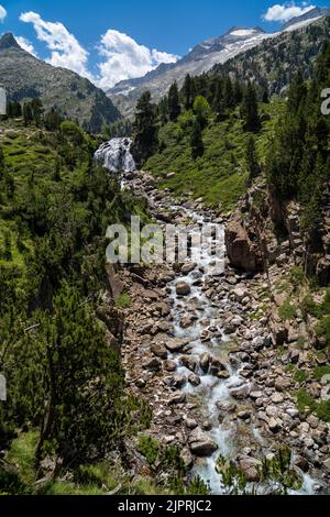 Spektakuläre vertikale Aussicht Fluss mit großen Steinen aus einem Wasserfall in den aragonesischen Pyrenäen von Benasque. Berge und Wolken im Hintergrund Stockfoto