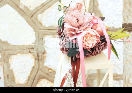 Schönes Vintage Bouquet mit Bändern und Spitze auf Kerzenlaterne gegen steinerne Mauerwerk Wand. Hochzeitsdekoration draußen. Große Kerzenlaternen mit Pin Stockfoto