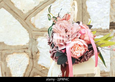 Schönes Vintage Bouquet mit Bändern und Spitze auf Kerzenlaterne gegen steinerne Mauerwerk Wand. Hochzeitsdekoration draußen. Stockfoto