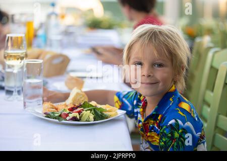 Süßes Kind, das im Sommer im Restaurant im Freien sitzt und Meeresfrüchte, Garnelen, Calamari, Tintenfisch und pommes frites isst Stockfoto