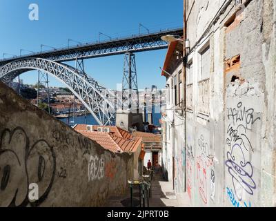 Treppensteig führt zum Douro River mit Luis I-Brücke, die sich über dem Fluss erhebt. Die Wände sind mit Graffiti bedeckt. Porto, Portugal. Stockfoto