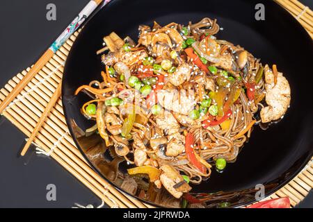Udon-Nudeln mit Fleisch, Pilzen und Gemüse. Mit Sesamsamen bestreut. Asiatische Lebensmittel, Braten auf schwarzem Hintergrund, Kopierraum Stockfoto