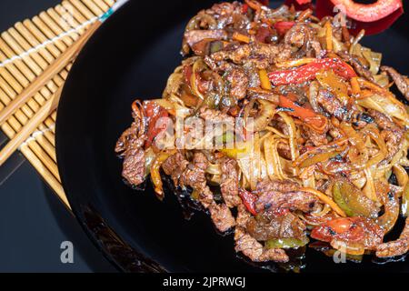 Udon-Nudeln mit Fleisch, Pilzen und Gemüse. Mit Sesamsamen bestreut. Asiatische Lebensmittel, Braten auf schwarzem Hintergrund, Kopierraum Stockfoto