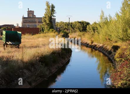 Blick auf den Canal de Pisuerga entworfen, um die zu bewässern Ackerland in Lantadila Palencia Spanien mit einem alten Bauerntrailer Und die Kirche Stockfoto