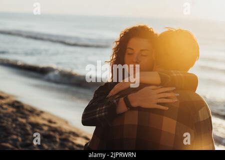 Junge Frau und Mann, ein süßes Paar, das sich vor dem Hintergrund des Meeres und der Sonnenstrahlen in der Dämmerung umarmt Stockfoto
