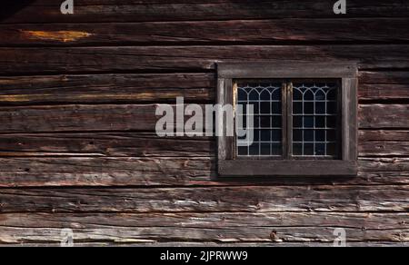Elegante Fenster mit Paneelverglasung an einer hölzernen Holzwand. Kraftvolles Holz und Blockbau in Nahaufnahme. Stockfoto