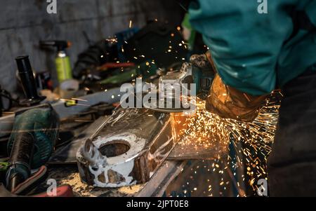 Mann, der in der Werkstatt mit Drehwinkelschleifer arbeitete, Details aus der Nähe, orangefarbene Funken flogen herum Stockfoto